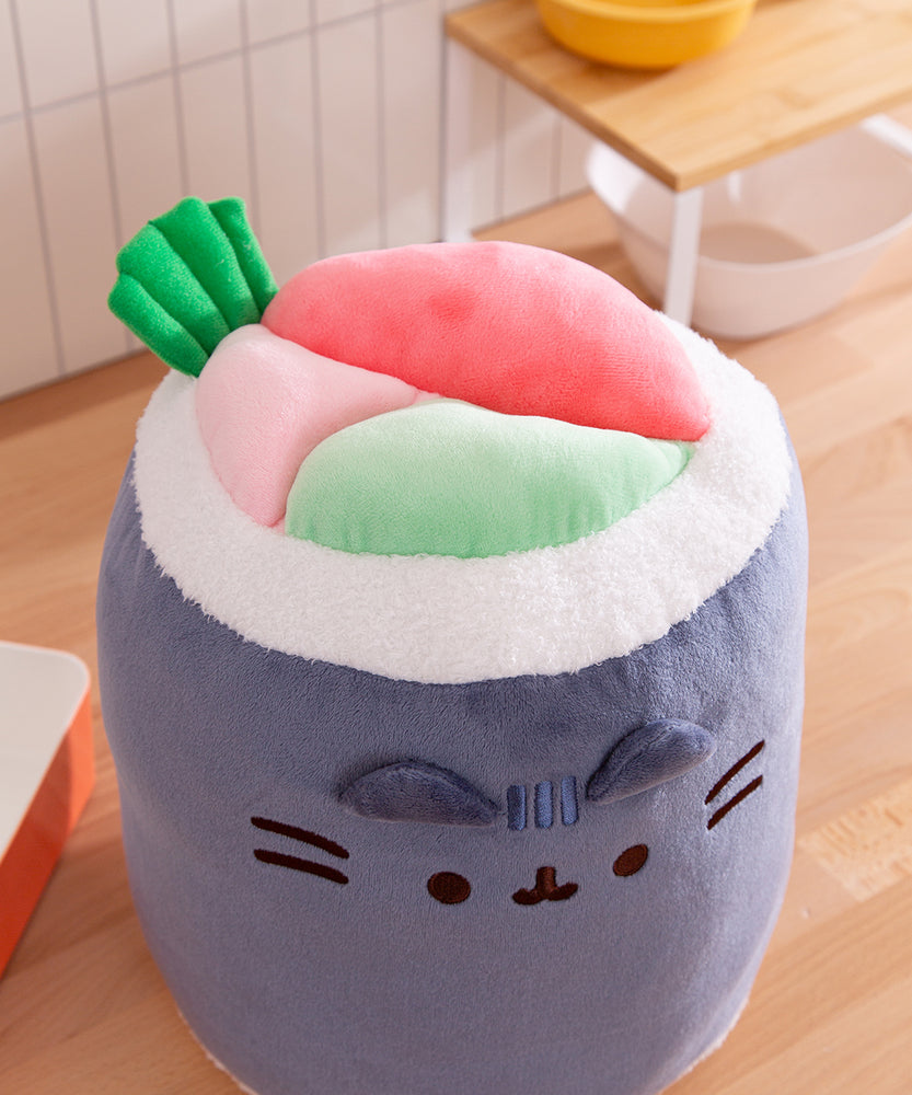 Pusheen Sushi Roll Plush sits on a table top. The seaweed and rice plush is wrapped around green and pink fillings.