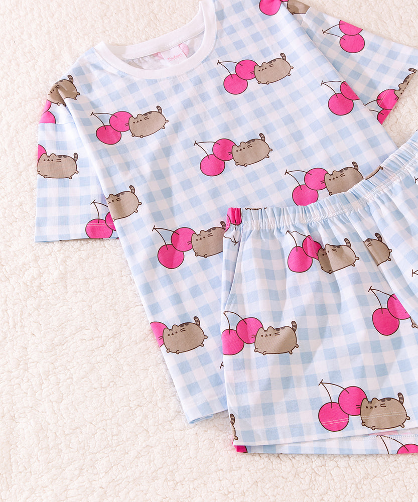 Cherry Pajama Set includes a light blue and white patterned short sleeve shirt with Pusheen graphics with pink cherries that match the pattern of the blue and white lounge shorts.  The shorts have side pockets and an elastic band top for a perfect fit.