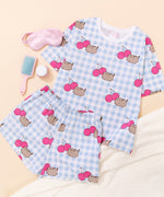Pusheen Cherry Pajama Set includes a white and blue gingham oversized top and elastic waistband shorts. The set has an all over print of Pusheen the Cat leaping next to two dark pink cherries. 