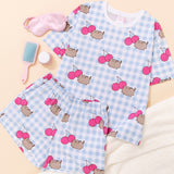 Pusheen Cherry Pajama Set includes a white and blue gingham oversized top and elastic waistband shorts. The set has an all over print of Pusheen the Cat leaping next to two dark pink cherries. 