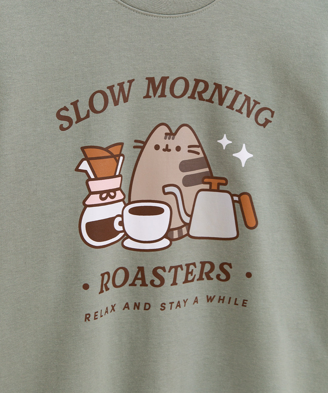 Close-up of the large graphic on the front of the Pusheen Coffee Sweatshirt. The text on the sage green sweater says "Slow Morning Roasters" and "relax and stay awhile".
