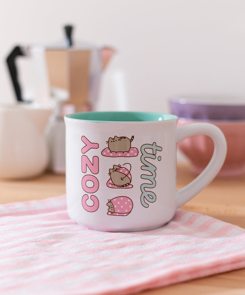 Close-up of the printed pink, white, grey, brown, and mint green graphic on the Pusheen Cozy Time mug that has a white exterior and green interior.