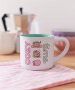 Close-up of the printed pink, white, grey, brown, and mint green graphic on the Pusheen Cozy Time mug that has a white exterior and green interior.