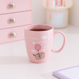 Pink Pusheen mug with a design of Pusheen the Cat floating in the clouds while attached to a pink balloon. In the clouds is the phrase 'enjoy every day'.