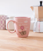 Pink Pusheen Enjoy Every Day Mug shows Pusheen the Cat floating in the white fluffy clouds with the phrase 'enjoy every day'.