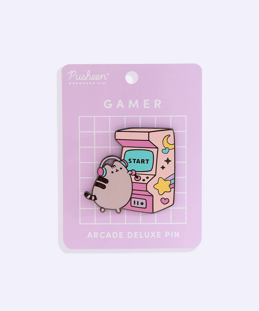 Front view of the Pusheen Gamer Arcade Deluxe Pin on its purple backer card. A grey cat stands to play a pink retro arcade game. 