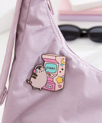 Close-up of the Pusheen Gaming Pin on a purple purse. The arcade game is two-toned pink and features yellow stars and moons.