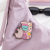 Close-up of the Pusheen Gaming Pin on a purple purse. The arcade game is two-toned pink and features yellow stars and moons.