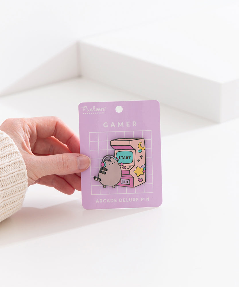 Model holds edge of backer card of the Gamer Pusheen Deluxe Pin to show the size and scale of the pin's details. 