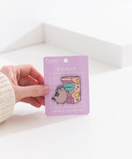 Model holds edge of backer card of the Gamer Pusheen Deluxe Pin to show the size and scale of the pin's details. 