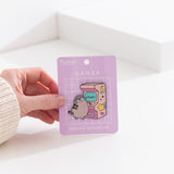 Model holds edge of backer card of the Gamer Pusheen Deluxe Pin to show the size and scale of the pin's details. 