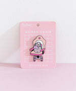 Front view of the Pusheen Gamer Chair Deluxe Pin on its pink backer card. A grey cat sits in an oversized chair to play online games.