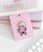 Front view of the Pusheen Gamer Chair Deluxe Pin on its pink backer card. A grey cat sits in an oversized chair to play online games.