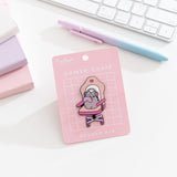 Pusheen Gamer Chair Deluxe Pin on a pink backer card. The large pin features Pusheen the Cat sitting in an oversized gaming chair with wearing a headset and holding a purple gaming controller.
