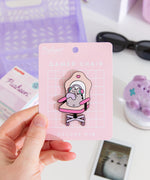 Model holds edge of backer card of the Gamer Pusheen Deluxe Pin to show the size and scale of the pin's details. 