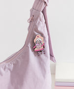 Close-up of the Pusheen Gaming Pin on a purple purse. A cartoon cat sits in a pink and purple desk chair while playing video games.