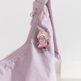 Close-up of the Pusheen Gaming Pin on a purple purse. A cartoon cat sits in a pink and purple desk chair while playing video games.