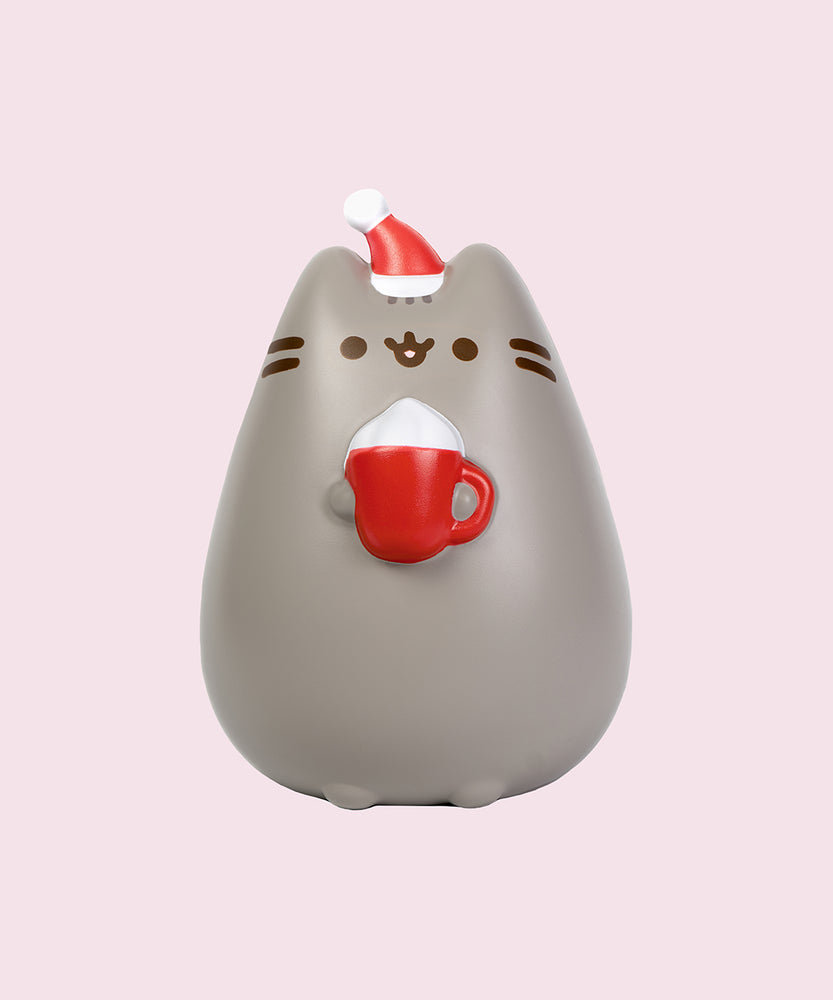 Front view of the Pusheen Holiday Jumbo Squishy. The gray cat is wearing a white and red santa hat while holding a red mug with white whipped cream.
