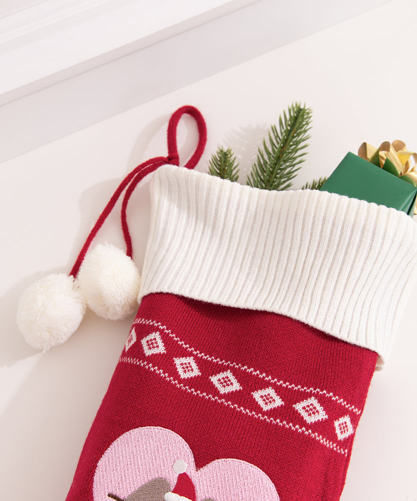 Close-up of the white ribbed top at the top of the stocking. Attached to the ribbed top is a red hanging loop with two white pom poms attached to red string.