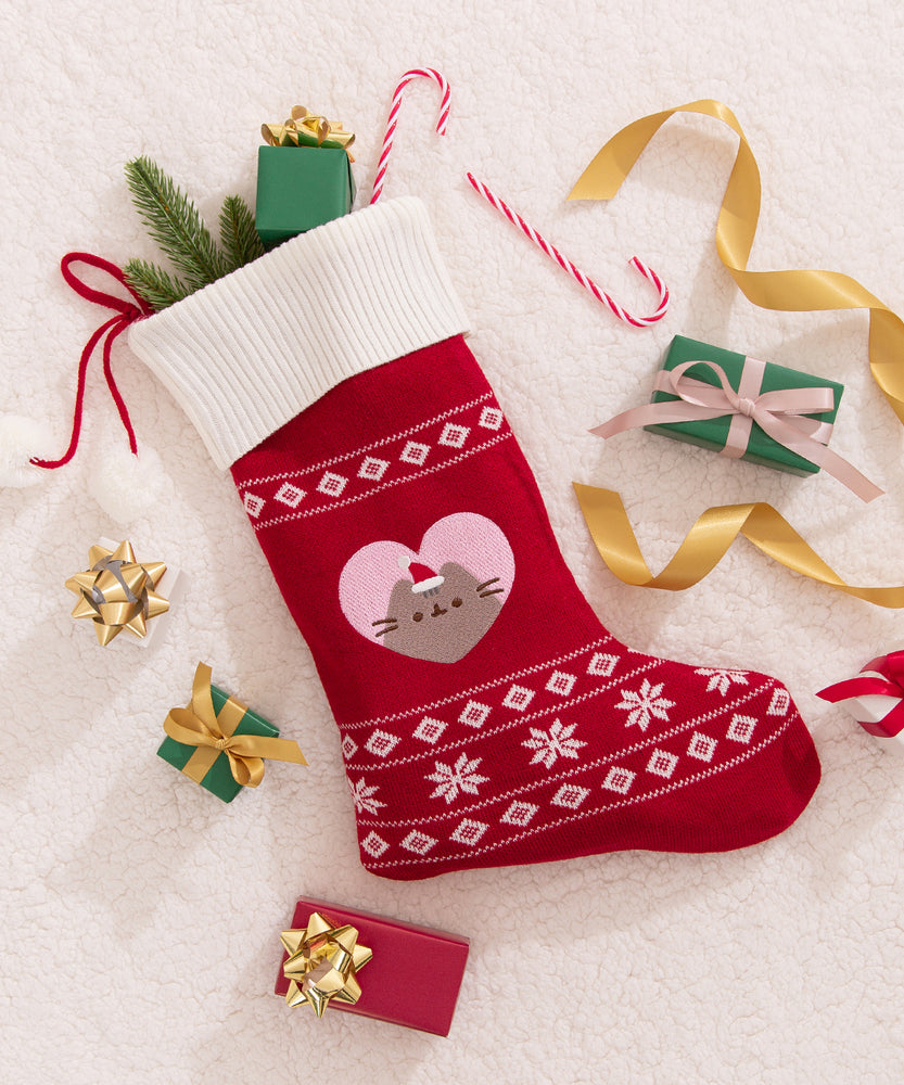 Pusheen stocking with a heart design in the middle of the knit stocking. The red holiday stocking is surrounded by holiday packages and ribbon.