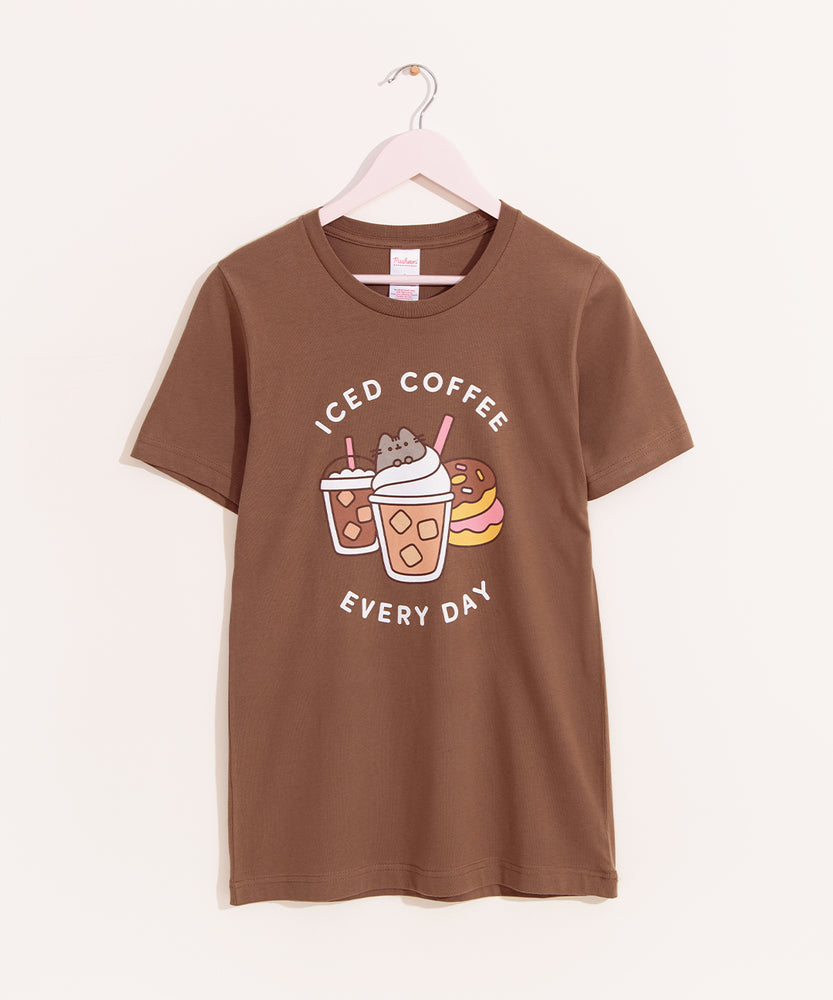 Pusheen Iced Coffee Tee hangs on a light pink hanger on a light background. The medium brown tee shirt has a graphic of Pusheen the Cat atop her favorite iced coffee beverages and some donuts.