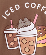 Coffee t-short lies on a flat surface. The brown tee has a large graphic in the center front of the t-shirt feauring Pusheen the Cat, two iced coffees, two iced donuts, and the phrase "Iced Coffee Every Day."