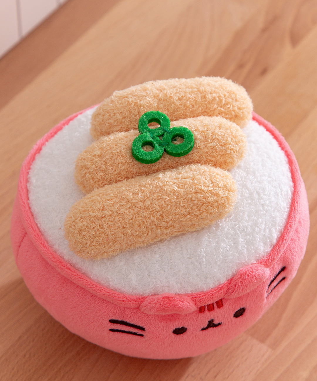 Aerial view of the toppings on the rice bowl plush that includes three green chopped scallion pieces and three tempura pieces atop a mound of white rice.