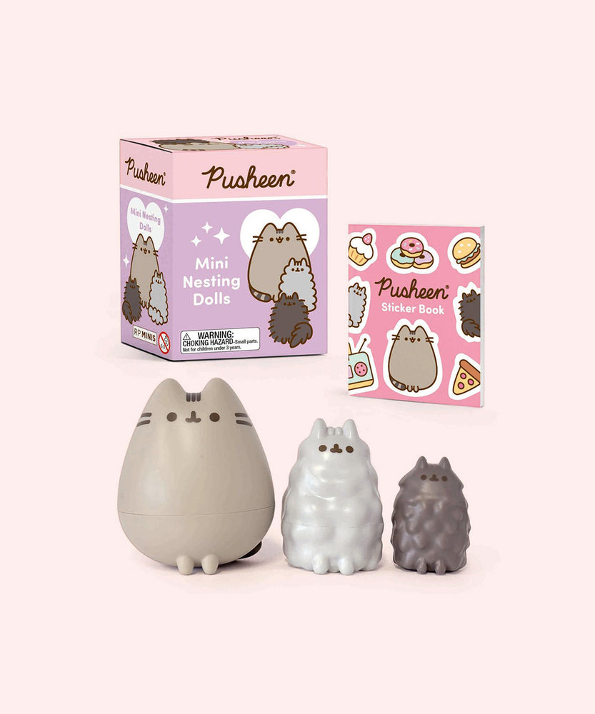 Pusheen Mini Nesting Dolls set featuring Pusheen, Stormy, and Pip sit in front of the packaging box that the dolls come in and the included sticker book.