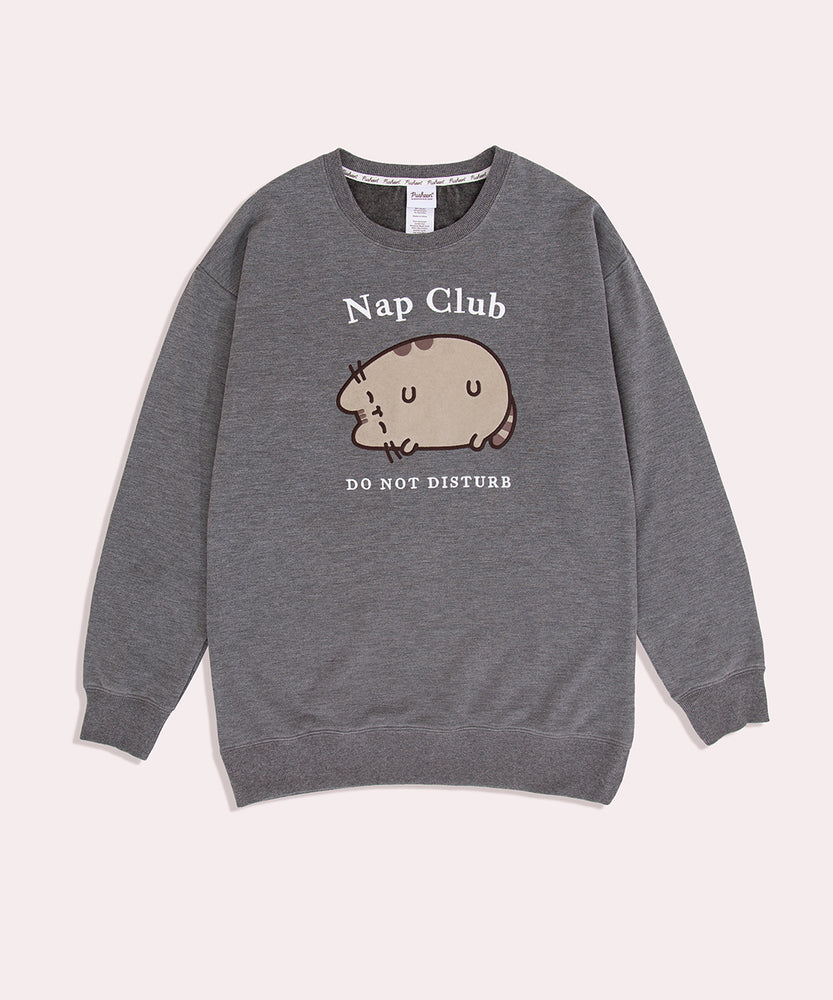 Pusheen Nap Club Loungewear Sweater lies on a flat surface. The gray sweatshirt features Pusheen’s face on the front in a flocked material.