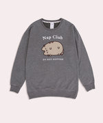 Pusheen Nap Club Loungewear Sweater lies on a flat surface. The gray sweatshirt features Pusheen’s face on the front in a flocked material.