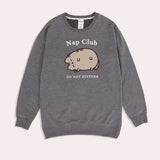 Pusheen Nap Club Loungewear Sweater lies on a flat surface. The gray sweatshirt features Pusheen’s face on the front in a flocked material.