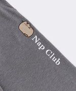 Close-up of the embroidered Pusheen graphic going down wearer's pant leg. The embroidery thread color is white and says "Nap Club" next to a graphic of a sleeping Pusheen.