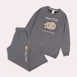 The Pusheen Nap Club Loungewear Set lies on a light background. The set includes a sweatshirt with an embroidered cat face on the front.  The set also includes gray pants that are folded in this image. 