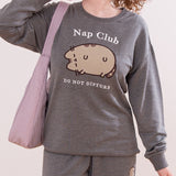 Close-up of front graphic on gray sweatshirt. Pusheen the Cat is shown in a flocked fabric and the phrases "Nap Club" and "Do Not Disturb" are embroidered in white.