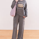 Model wearing Pusheen Loungewear Set. The grey outfit includes a sweatshirt and matching pants. The model is carrying a purple purse.