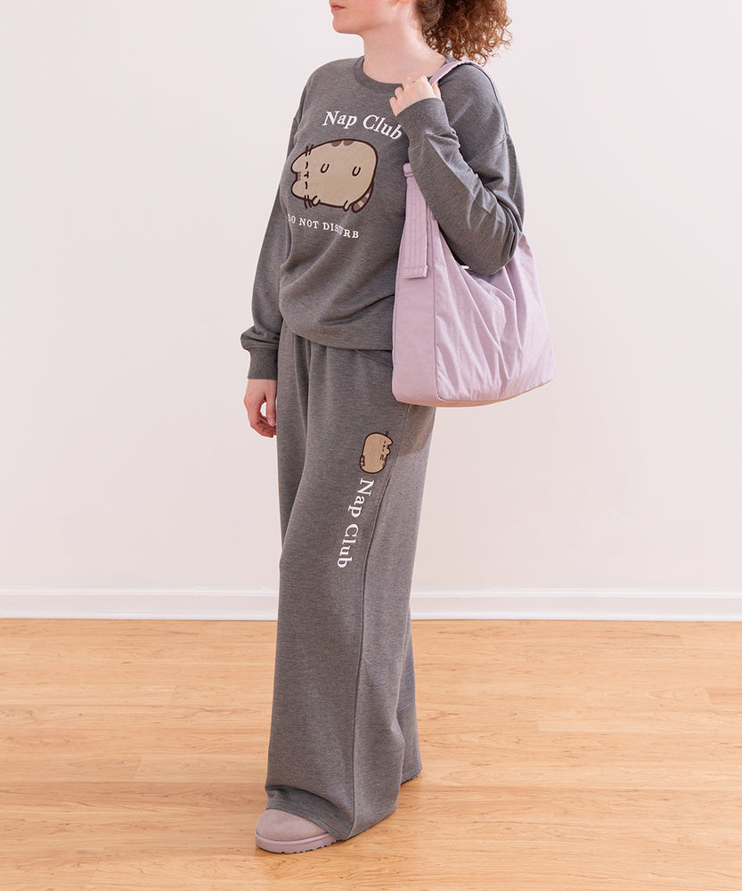 Pusheen Nap Club Loungewear Sweater lies on a flat surface. The gray sweatshirt features Pusheen’s face on the front in a flocked material.