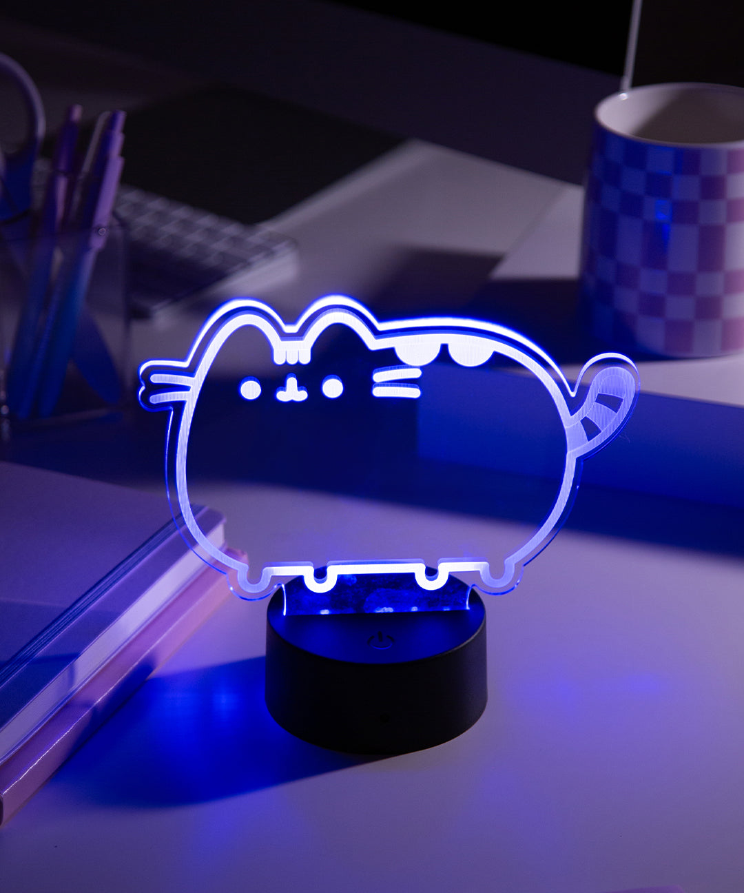 Purple LED light shaped like Pusheen the Cat on a desk with a laptop and cup in the background.