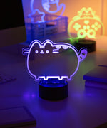 Pusheen Otaku Lamp light shaped like a cat on a desk with other neon lights in the background.