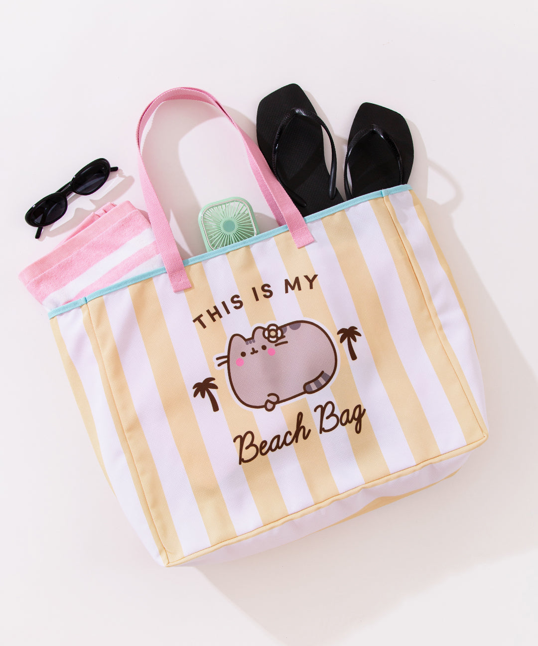 Pusheen Oversized Beach Tote Bag lies on a surface and shows a beach towel, fan, and sandals inside the extra roomy bag.
