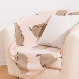 Pusheen Blanket draped over a cream arm chair with a pillow on top.