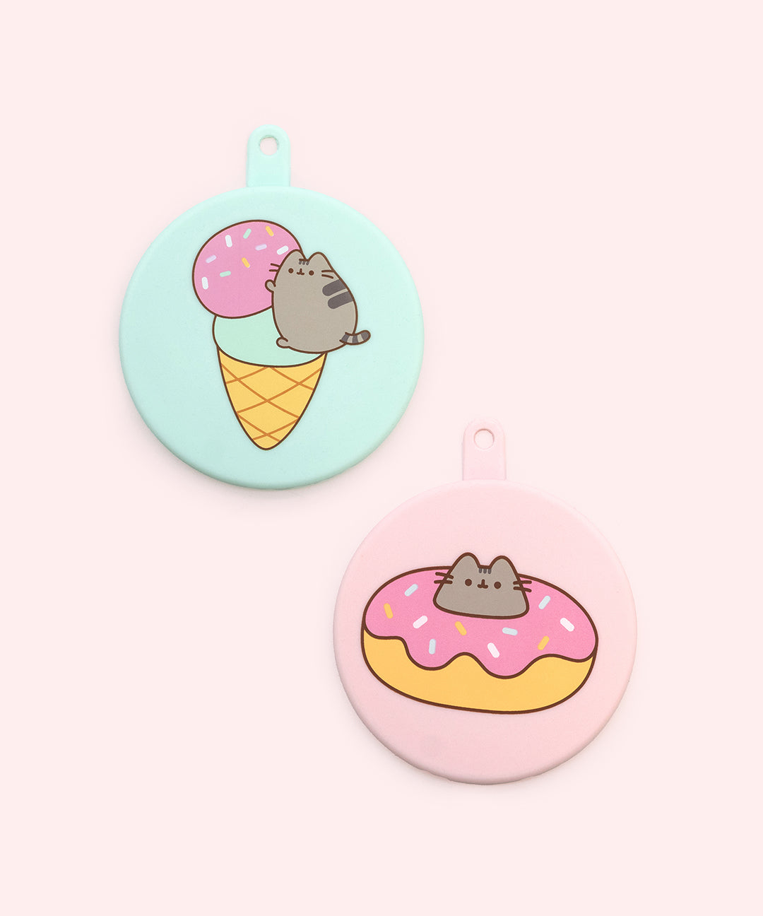 Close-up of the pink and mint green Pusheen pet food can covers. The two silicone can covers have graphics printed on the top of Pusheen with sweet treats including a donut and ice cream cone.
