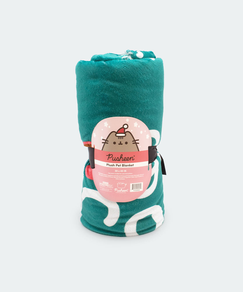 The Holiday Pet blanket is rolled inside its packaging which states that it is a “Pusheen Plush Pet Blanket.” The packaged green blanket sits in front of a light background. 