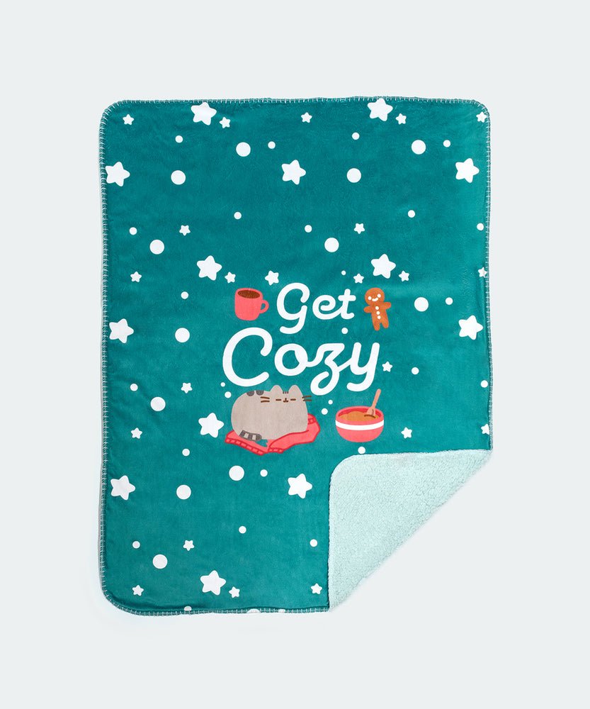 The Holiday Pet blanket is rolled inside its packaging which states that it is a “Pusheen Plush Pet Blanket.” The packaged green blanket sits in front of a light background. 