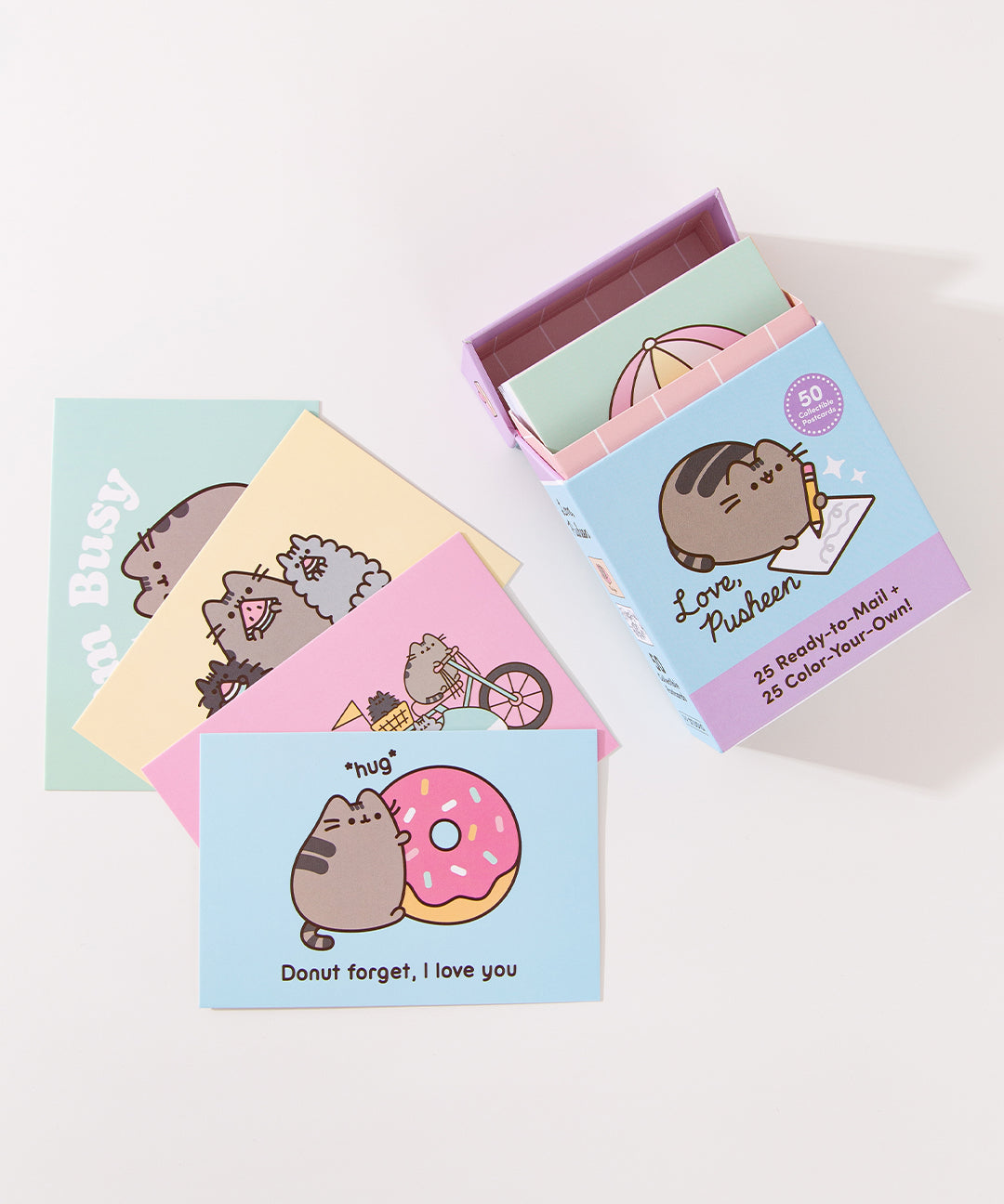 Set of Pusheen-themed illustrated postcards cards next to their keepsake box on a white background.