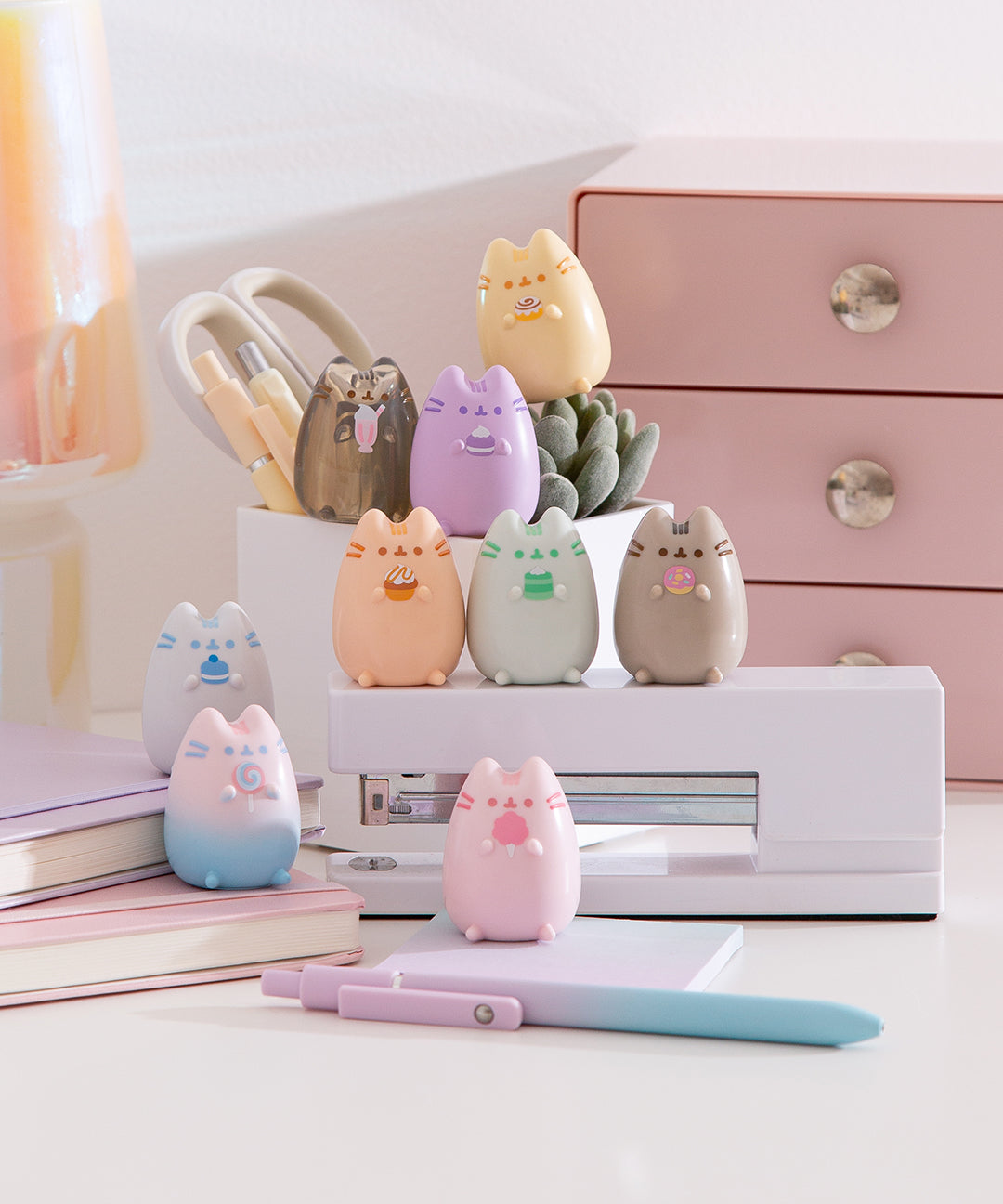 Pastel-colored cat-shaped figurines sit on a desk surrounded by stationery.