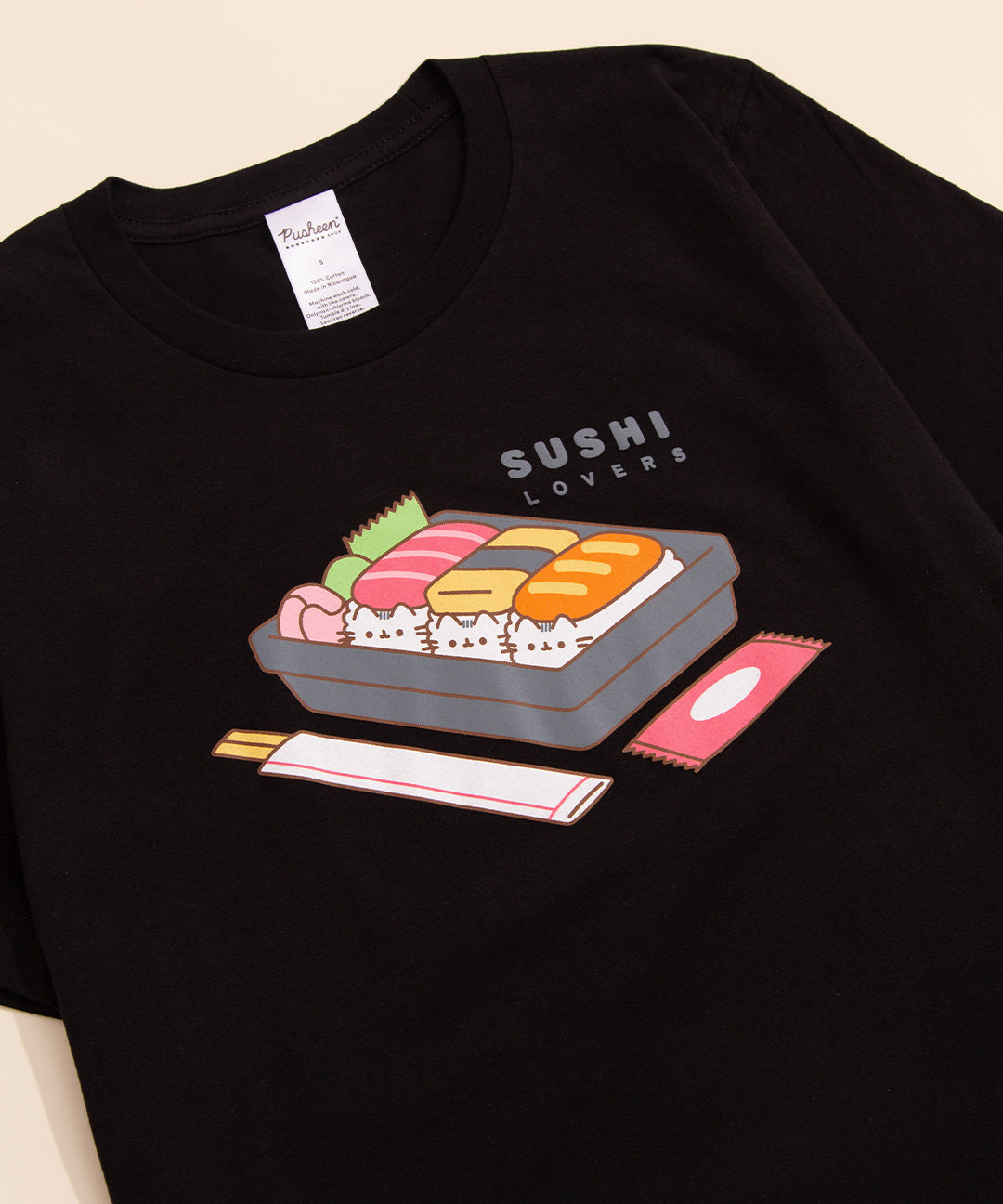 Close-up of the graphic on the black Pusheen t-shirt with a sushi in a container and the phrase "sushi lovers" above
