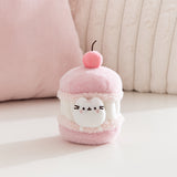 Cat plush toy resembling a macaron with a cherry on top, sitting on a light pink surface. A white Pusheen the Cat mini plush is able to removed from the macaron plush environment. 