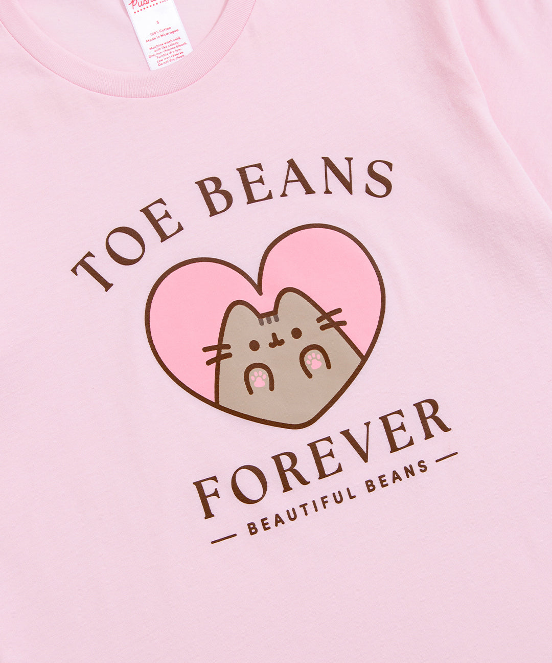 Close-up view of toe beans pink graphic tee. The phrases surrounded Pusheen the Cat in a brown font are "Toe Beans Forever" and "Beautiful Beans."