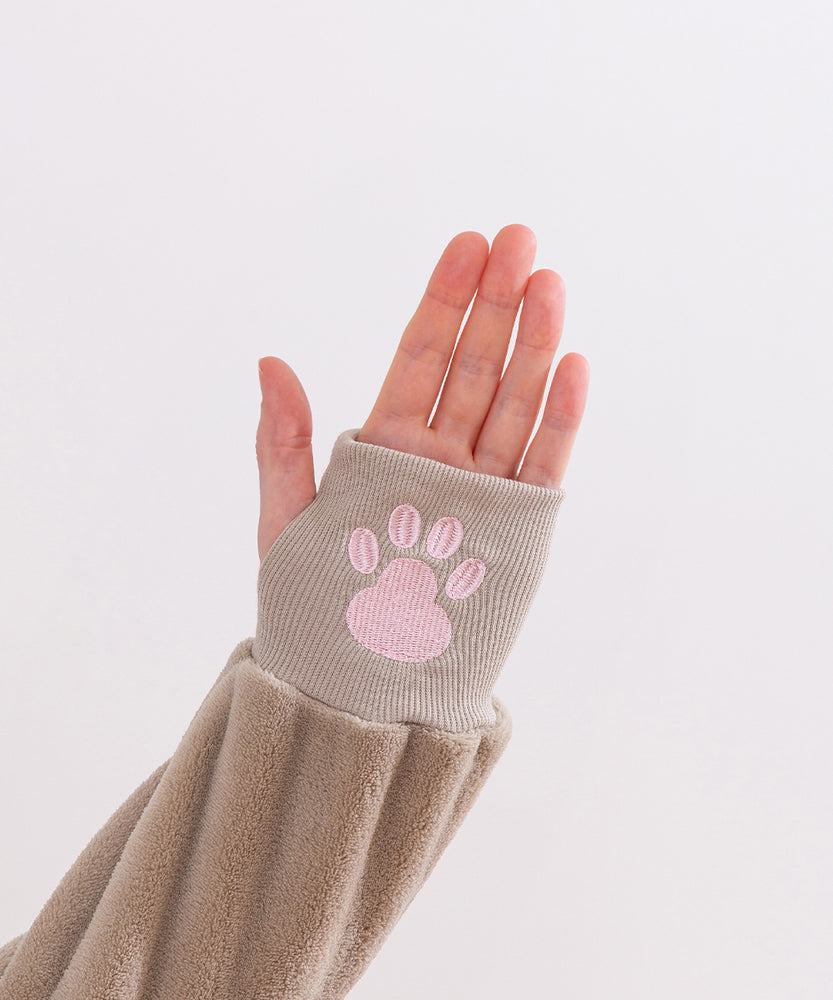 Model's hand with thumb through thumb hole on the Toe Beans Kigurumi. A pink paw print is embroidered on the ribbed cuff.