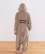 Model wearing a fleece onesie with a hood up. The back gray stripes, grey and brown striped tail, and pink paw print embroidery can be seen in this image.